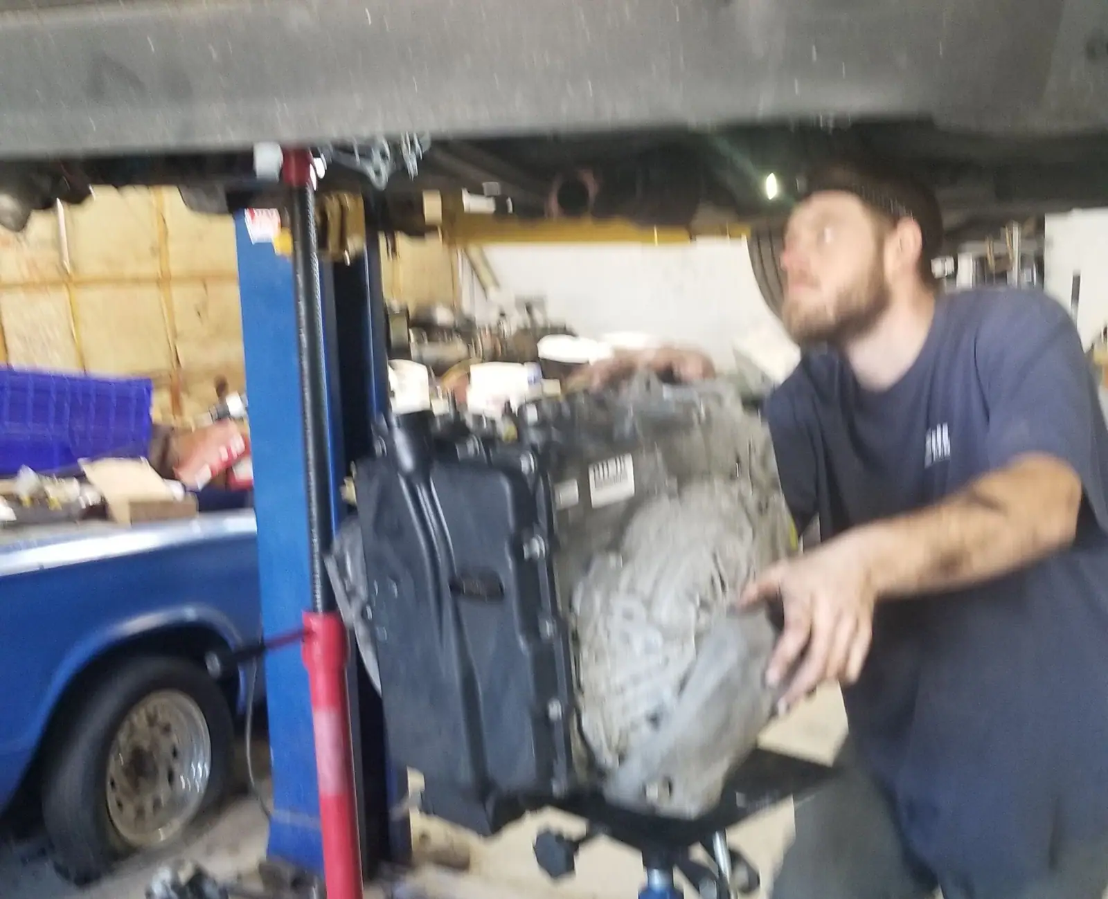 J&W mechanic guiding a transmission down on a jack under a raised vehicle
