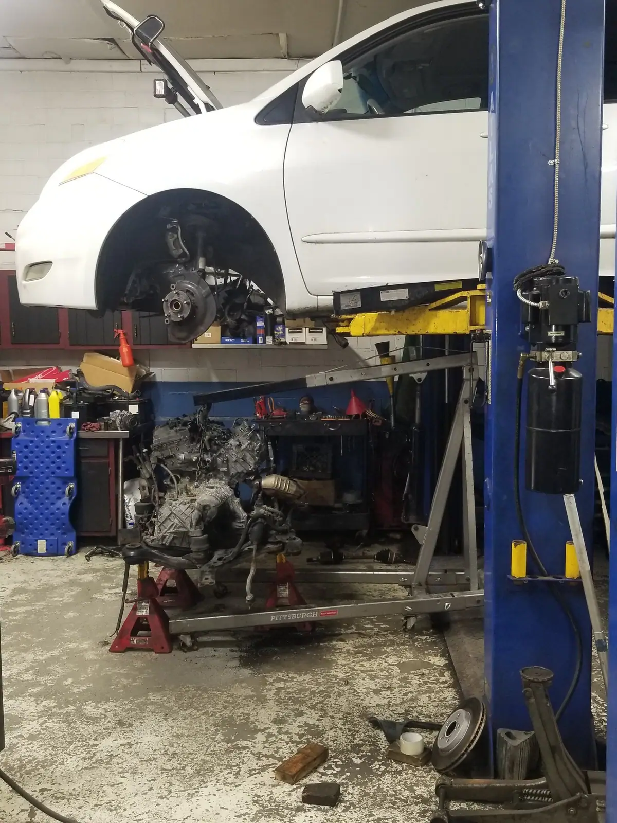 White car on the lift with its engine and transmission lowered out on a crane
